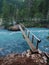 A narrow footbridge crosses over blue glacial water in the Canadian Rockies