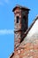 Narrow old dark red bricks dilapidated cracked chimney partially covered with concrete and small roof tiles on top