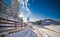 Narrow road covered by snow at countryside. Winter landscape with snowed trees, road and wooden fence. Cold winter day at village