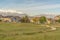 Narrow road and grassy terrain against homes and snowy mountain on a sunny day