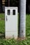 Narrow small locked grey plastic electrical meter and fuse box next to tall concrete utility pole in suburban family house