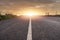 Narrow straight asphalt road with white road markings at sunset. Dramatic sky. Nobody. Low angle of view. Travel concept