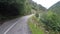 Narrow winding road in mountains surrounded by trees, dangerous driving