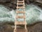 A narrow wooden bridge over a stormy icy river with rocky banks. View from above. Extreme river crossing