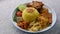 Nasi Kuning or Yellow rice with traditional fried chicken, tofu, tempeh, and smashed potato on blue background.