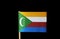 A national flag of the Comoros on toothpick on black background. Four horizontal stripes of yellow, white, red and blue with a gre