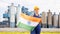National flag of India in the hands of girl in overalls against background of modern metallurgical plant
