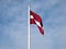 The national flag of Latvia in the wind with blue cloudy sky. Exact colours of Latvian flag - carmine red with white horizontal