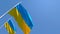 The national flag of Ukraine flutters in the wind against a blue sky