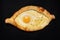 The national Georgian dish is Adjarian khachapuri. Open boat-shaped cheese and egg pie isolated on black background