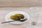 National trait is unhealthy:faceted glass Russian vodka on a white table, a couple of cucumbers laying on the plate, the plug is