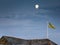 A National Trust flag flies high on a Cornish rooftop,with the silver moon shining beyond,against a darkening sky.