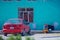 Native Indigenous old lady in traditional dress in colorful city street with car, in Mexico, America