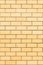 The natural background of the wall is made of yellow finishing bricks. Smooth brickwork of a modern building. A vertical fragment