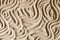 Natural beige sand texture background with wave pattern. Wavy curved ornaments on sand, drawn by hand. Top view