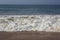 Natural copy space shot of a wave crushing on the smooth yellow sand beach surface, forming white foam, with the blue sky on the