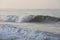 Natural copy space shot of a wave crushing on the smooth yellow sand beach surface, forming white foam, with the blue sky on the