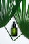 Natural cosmetic for beauty treatment. Green glass pipette bottle with essential oil or serum and palm leaves at white backdrop.