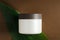 Natural cosmetic cream jar mockup on green leaf background. Makeup product blank container. Body care organic lotion, cleaning