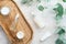 Natural cosmetics in transparent glass packaging with eucalyptus leaves and wooden plate on stone table in bathroom. Flat lay, top