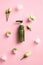 Natural face lotion in green dispenser bottle with ice cubes and flowers on pink background. Skincare concept