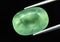 Natural gemstone green prehnite in tweezers on a gray background