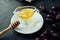 Natural honey in transparent saucepan with spout and wooden honey stick on saucer on dark table with dried dates scattered around