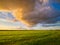 Natural landscape during sunset. Huge yellow clouds and blue sky. Field and meadow. Huge cloud in the sky after a storm.