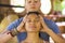 Natural lifestyle portrait of young beautiful and relaxed Asian Balinese woman receiving a healing facial and head Thai massage by