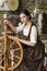 Natural Portrait of Young Brunette Girl Posing With Old Wooden Spinning Wheel in Retro Dress In Village Environment