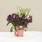 Natural Quail eggs in small pink bucket, colorful feathers in front of violet flowers, light rustic napkin on table