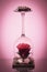 Natural rose flower in the flipped over wine glass with candle on reflective surface and gradient soft red background.