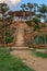 Natural stone stairway with green bushes on both sides leading to wooden pergola with partly cloudy sky at public Park in summer