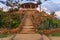 Natural stone stairway with green bushes on both sides leading to wooden pergola with partly cloudy sky in summer time