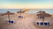 Natural straw sunshades on a deserted beach with large jetty going into the sea, bathed in warm evening sunshine - space for text