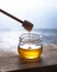 Natural vegan golden honey in a jar on wood background. The hand holds a stick, which drains the honey. Image is macro, close up a