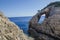 Natural window in stone in Korakonissi and people jumping in the water from a cliff