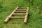 Natural wooden stairs lie on green grass on a clear day. Handcrafted light brown ladder lying on the ground. Design background.