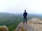 Nature hiker on sharp cliff roc watching over misty valley to blurred horizon. Terrible rainy weathe