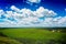 Nature landscape with green meadow, view from hill, bright blue sky with clouds