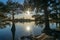 Nature landscape with sunset lake and sun shining through trees