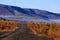 The nature of the Magadan region. Forest road among taiga during golden autumn. Dirt road