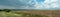 Nature panoramic landscape. Some wild flowers and green bush are growing on the edge of empty agricultural field. Blue