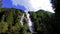 Nature View of a tall waterfall with Green Mountains and Blue Sky with white running clouds