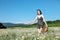 in nature, a woman with a hat runs into a field with daisies flowers