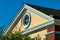 Nautical round window in attic room at pinnacle of home with beige stucco exterior and gable style roof white accents