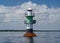 Navigation green buoy or beacon on in the calm blue sea water and cloudy sky