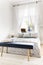 Navy blue bench with book and breakfast standing by the king-size bed in white bedroom interior with window with curtains