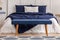 Navy blue velvet bench in the foot of king size bed in chic bedroom interior