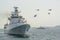 Navy warships running on sea while helicopter with flags flying